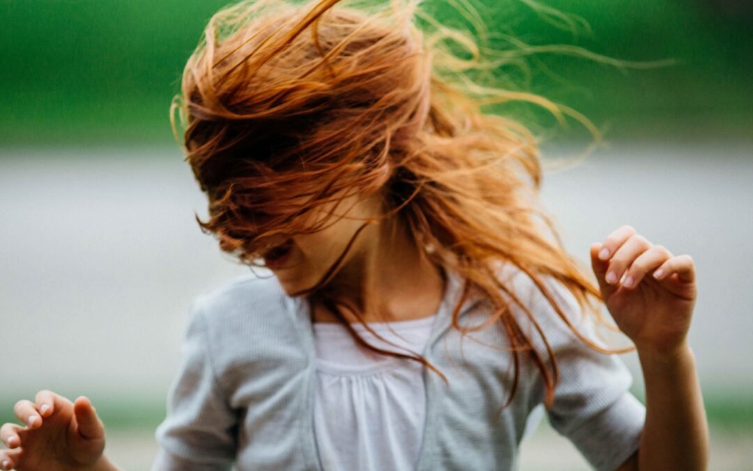 Young girl with red hair, dancing and laughing as she shakes her head and hair around.